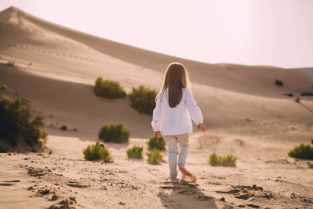 The back of a girl who walks towards the sand dunes in Dubai