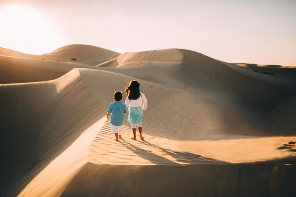 A little boy and her sister hold hands in the sand dunes of Abu Dhabi desert