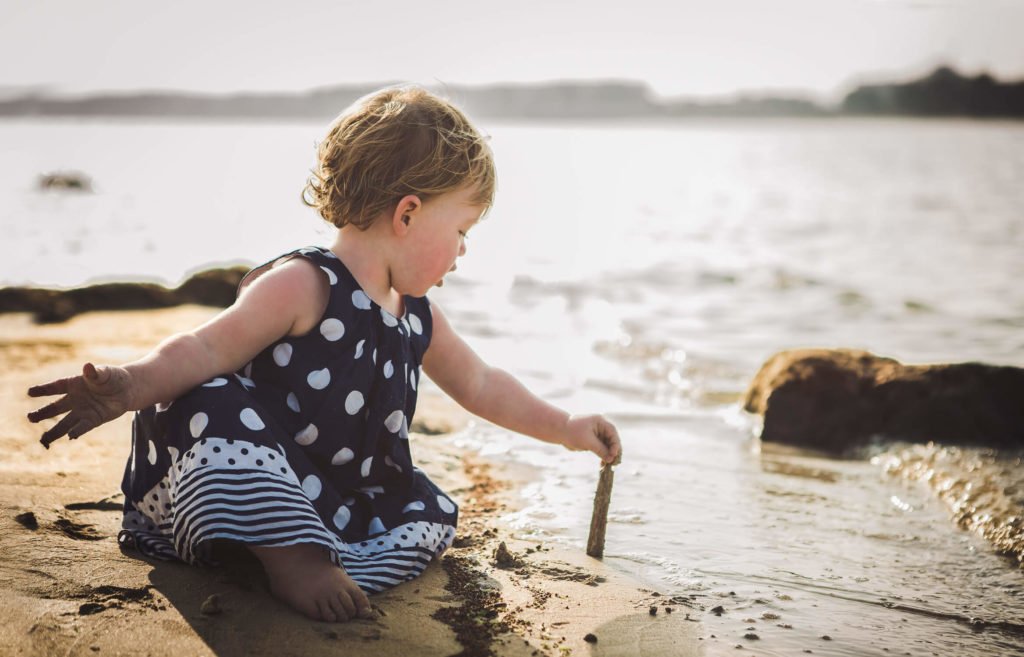 A little girl with her blue dress plays with a stick in the beach shore of Abu Dhabi