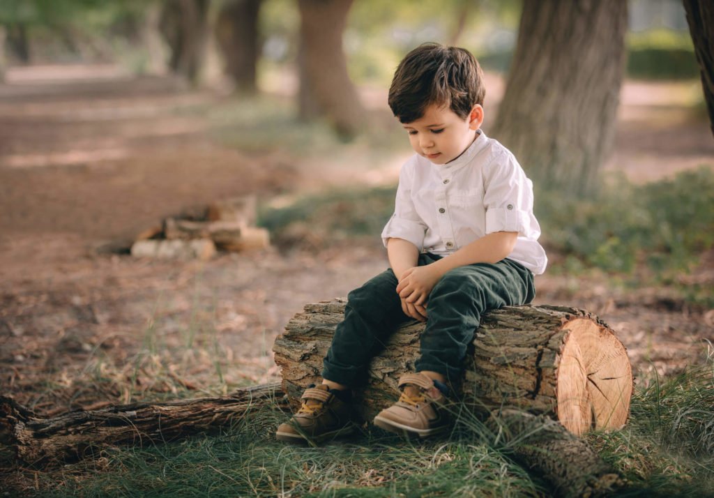 A toddler is sitting on a log at the park in Abu Dhabi