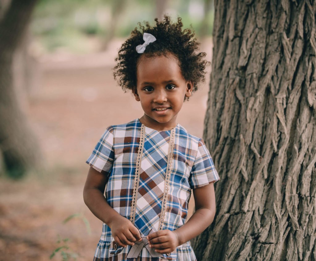 Portrait photography: A little beautiful black girl standing beside a tree