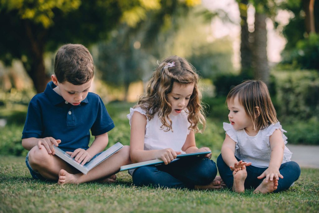 Three small children sitting in the grass reading a book in Dubai