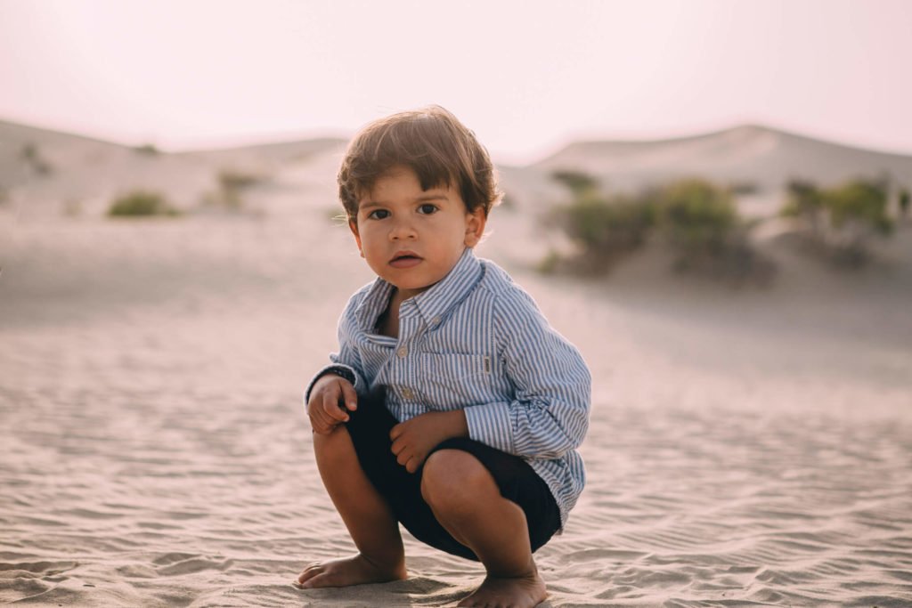 A toddler squats in the Abu Dhabi desert posing for his photographer