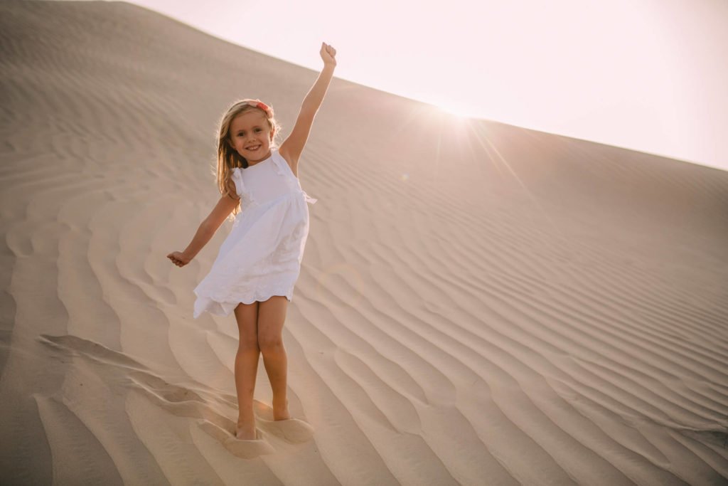 A girl in her white dress plays in the sand dunes of Abu Dhabi