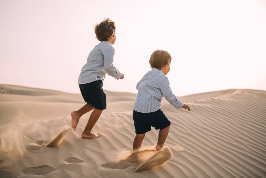 Two boys play in the sand dunes of Dubai desert