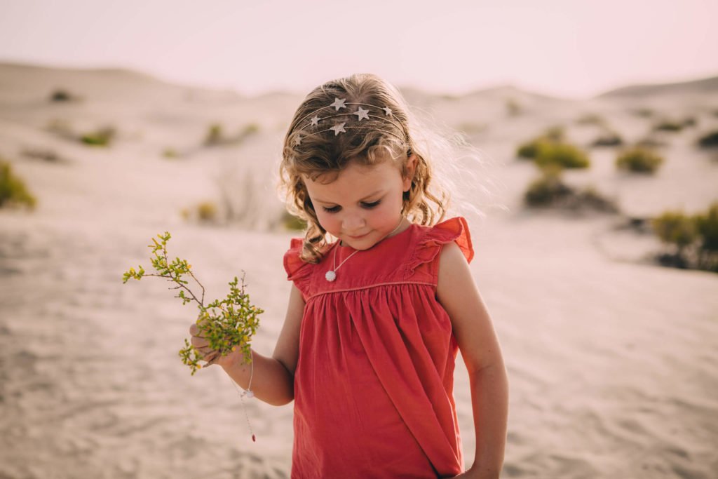 A girl with a red dress holds a desert flower in Dubai