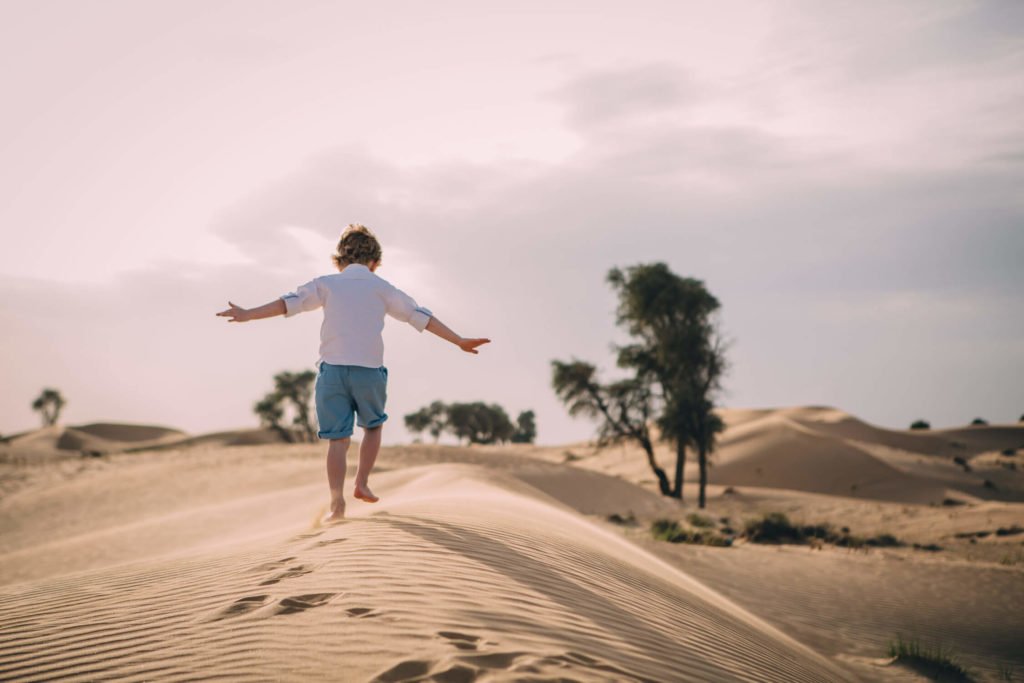 A boy pretends being an airplane in the sand dunes of Dubai