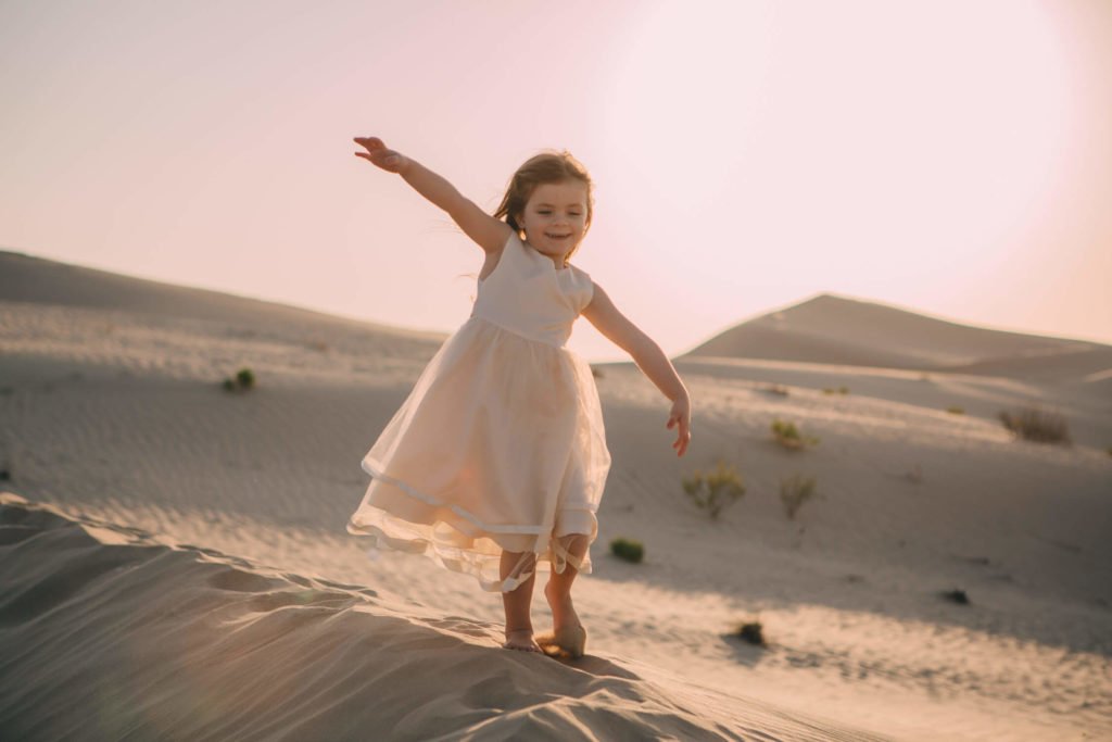 A girl in her cream dress pretends to fly in the sand dunes of Dubai desert