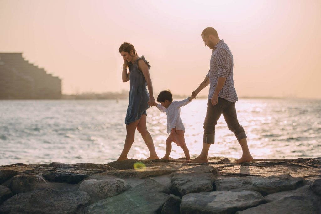 A mum, dad and their little son walking on the rocks with the ocean as a background. Family photographer Dubai