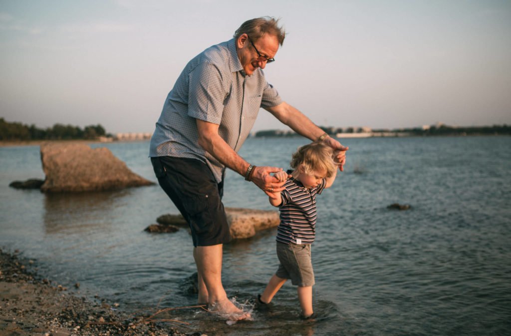 Grandfather holding the hands of the little boy while playing in the water. Abu Dhabi photographer