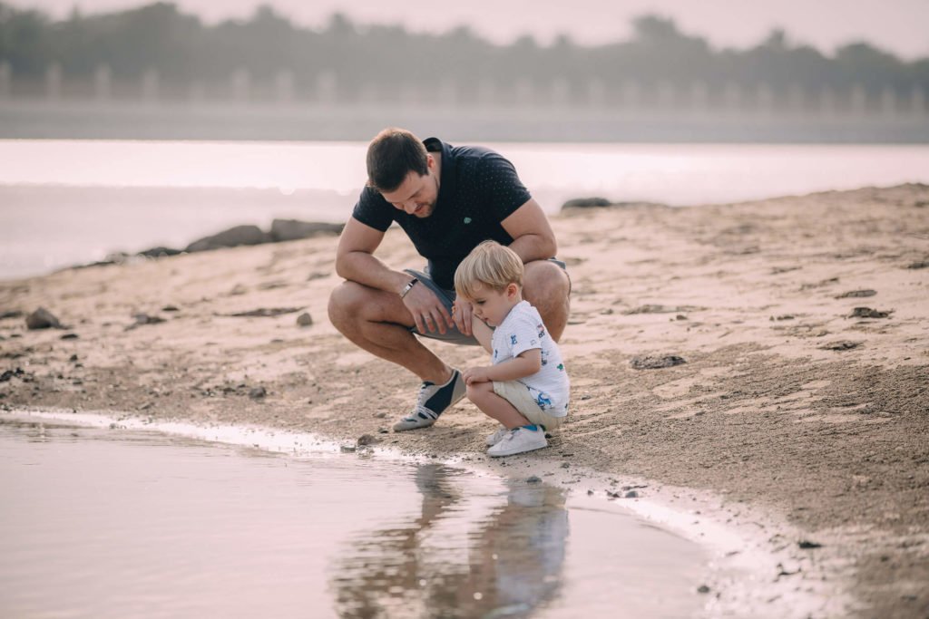 In Abu Dhabi a dad and her little boy squat while they look at the water in the beach