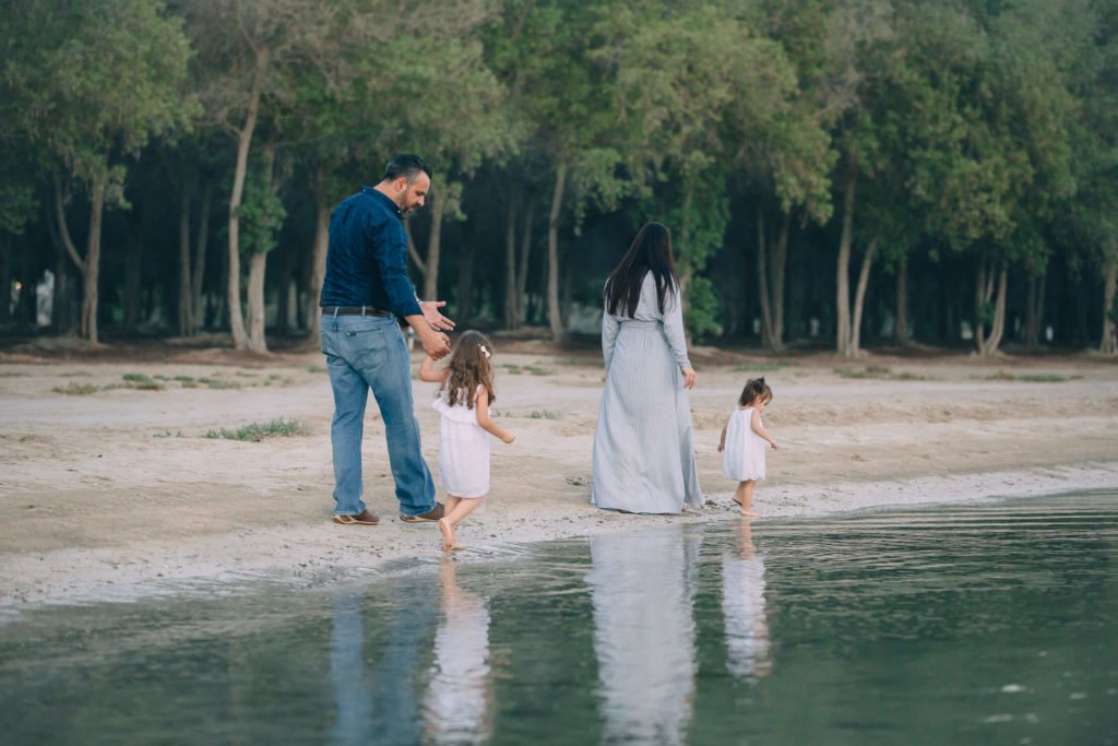Mum, dad and two girls having a walk by the shore of the beach.