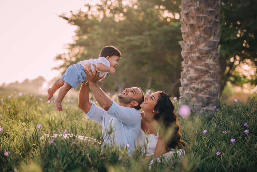 In Dubai a family surrounded by flowers, dad holds the baby boy up in the air and mum hugs her husband