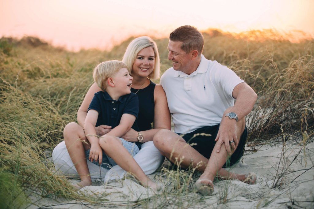 Mum holds her boy while him and his dad are laughing in the beach at sunrise