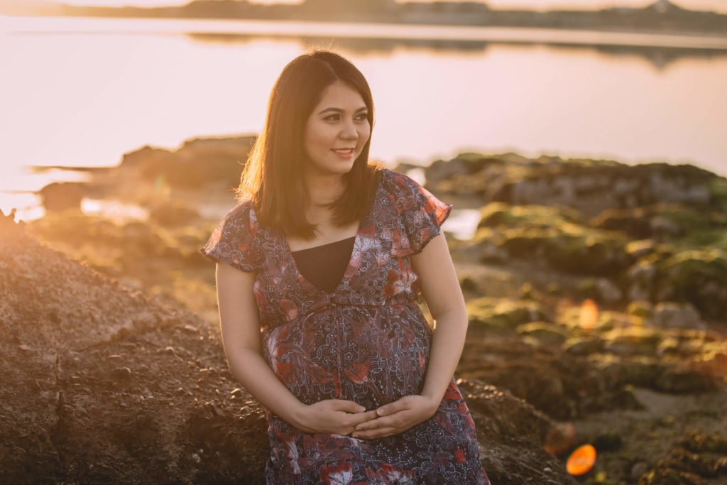 Pregnant woman sitting in the rocks at the beach during sunrise in Dubai