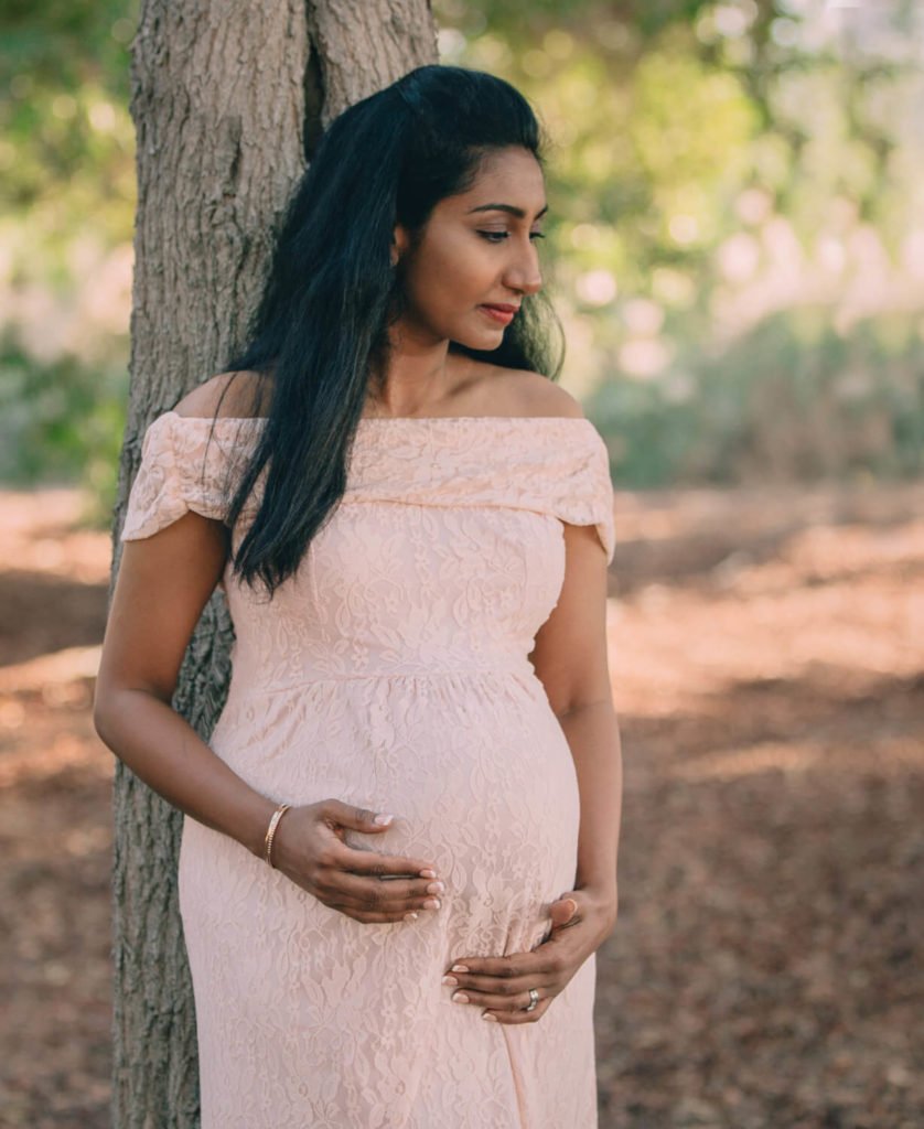 A woman is wearing a maternity gown and leaning on a tree in Abu Dhabi beach
