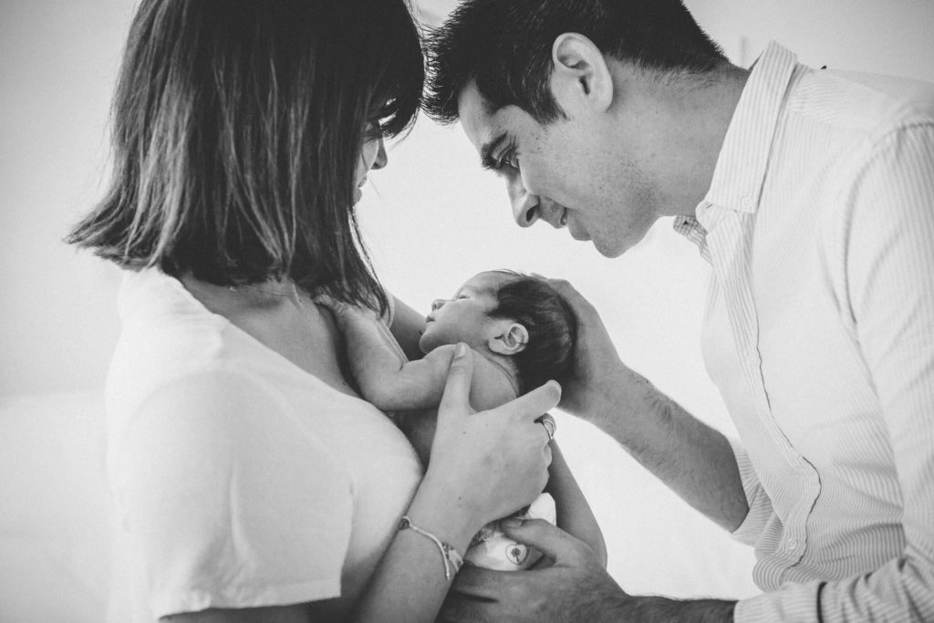 Mum carries the newborn while dad kisses his head