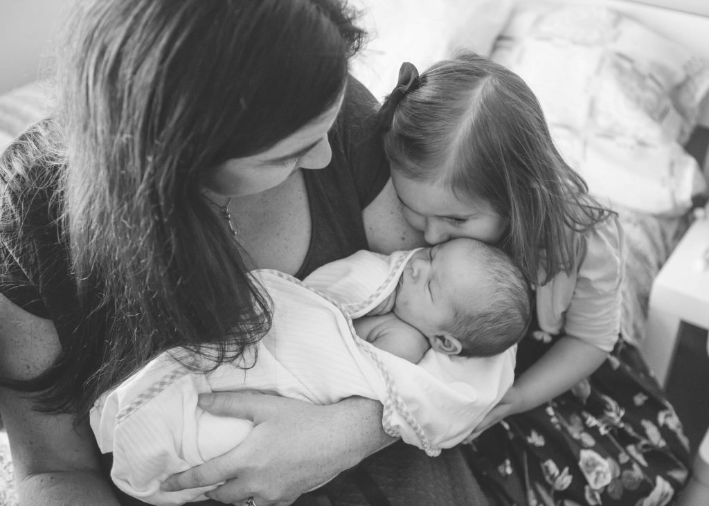 In Dubai a mother carries her newborn while her big sister gives her a kiss