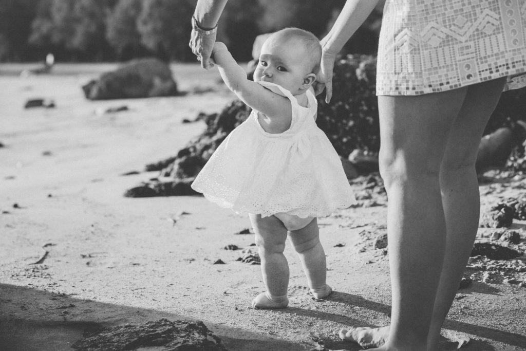 A mum holds hands of a baby girl to help her walk