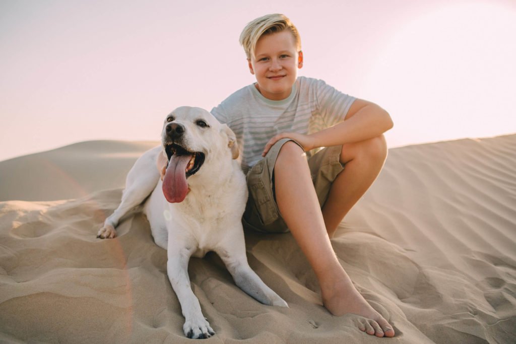 A boy and her white labrador play in the sand dunes of the Dubai desert