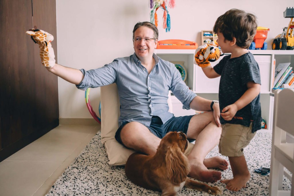 Dad and toddler play with their puppets while the dog looks at them