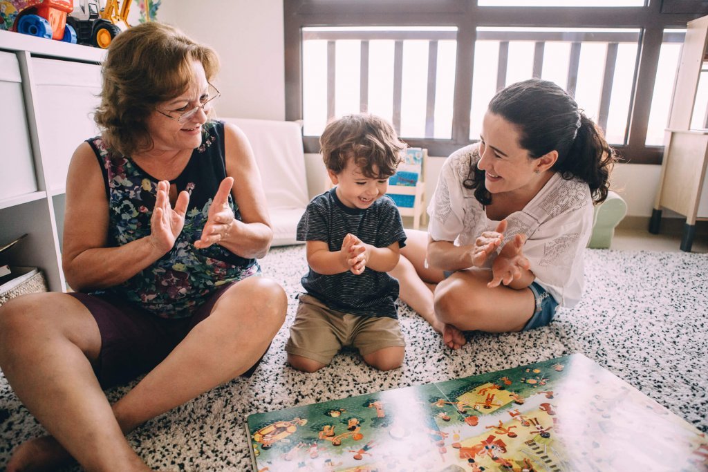In-home lifestyle family session. Grandmother, mother and little boy clap and smile