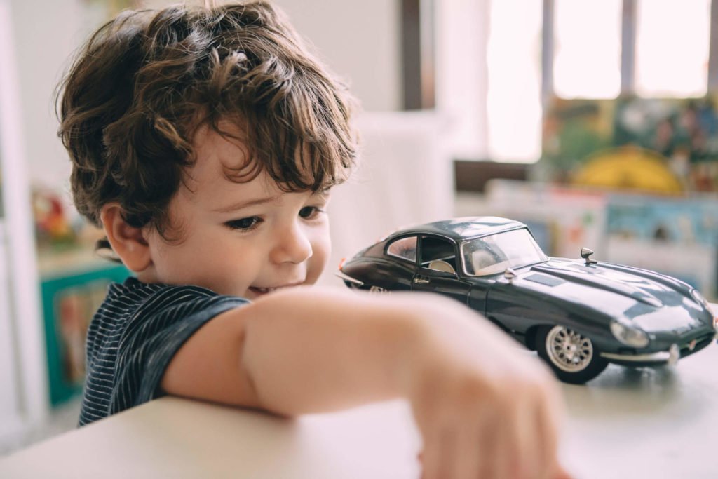 A little boy playing with his dark gray car