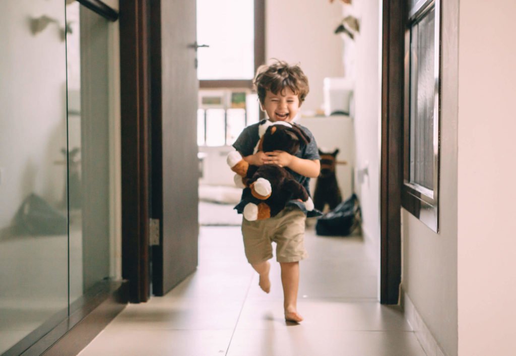 In-home lifestyle family session. A toddler runs out from his bedroom holding his stuffed dot
