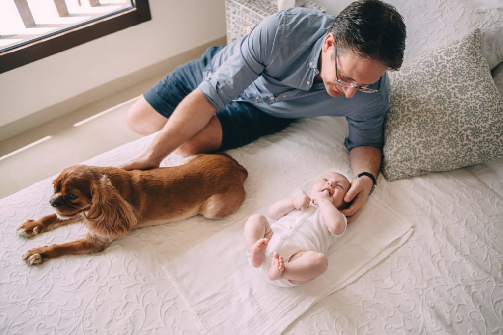 In-home lifestyle family session. Dad looks at his baby boy while softly touches his dog