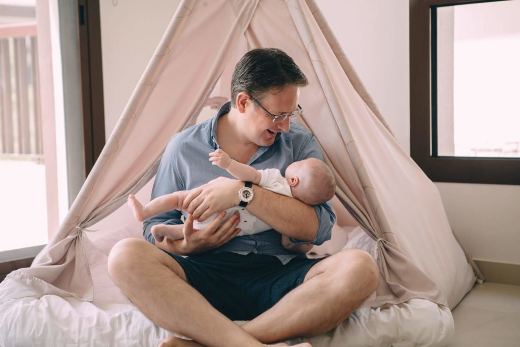 In-home lifestyle family session. A dad laughs at his baby boy sitting inside a teepee