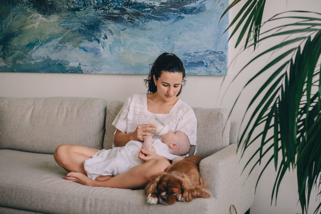 In-home lifestyle family session. Mum feeds her baby boy while her dog sits by her side