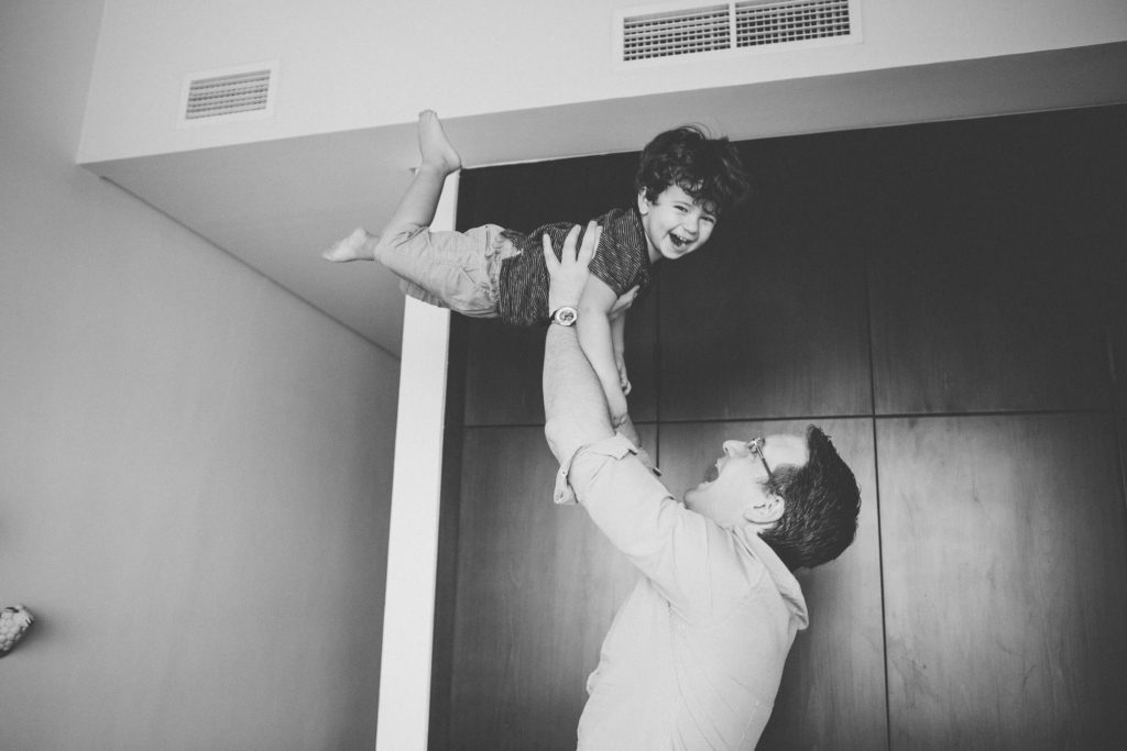 Dad has hold his toddler up in the air, while he laughs