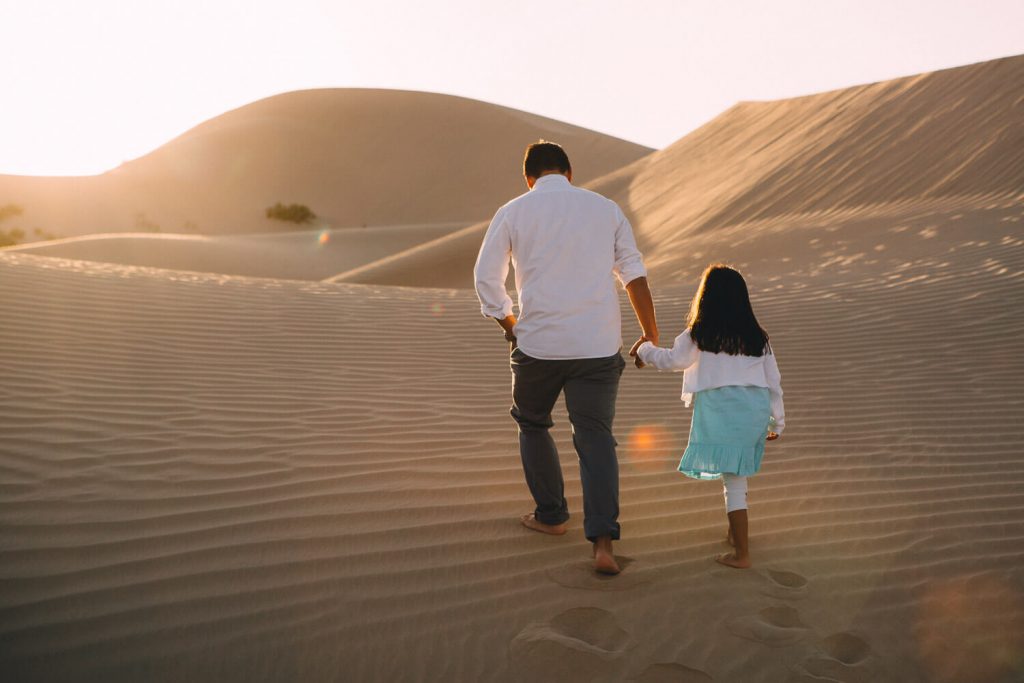 Desert photography in Abu Dhabi. Dad and daughter walking in the sand dunes